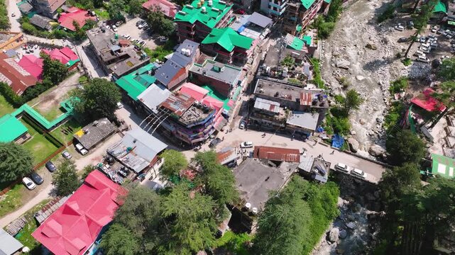 Aerial tilt-down onto the bustling town center of Kasol, highlighting the unique architecture and off-grid living of Himachal Pradesh.
