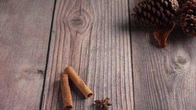 A hand in a warm grey sweater reaches into the frame to pick up a red mug of hot cocoa from a rustic wooden table decorated with winter spices