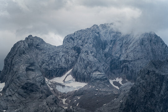 Majestic rocky mountain peak with glacier snow fields covered in moody clouds