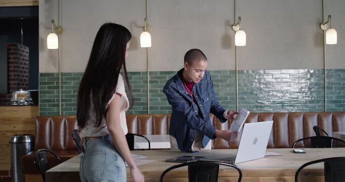 Diverse female coworkers meeting over files at cafe, denim jacket presenter opening laptop
