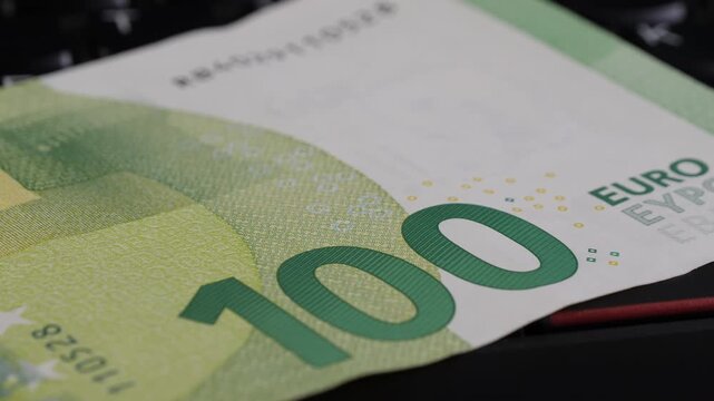 Close-up view of a 100 Euro banknote resting on a black keyboard, highlighting intricate design elements and textures, with the banknote positioned at an angle for visual emphasis