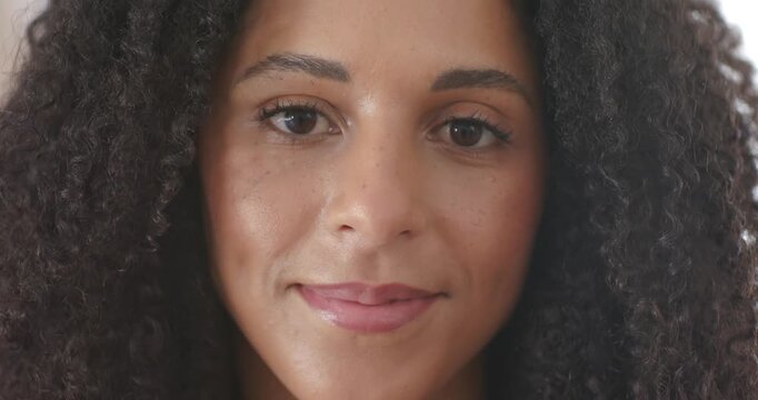 African American woman facing camera blinking smiling leaning closer in neutral room to connect