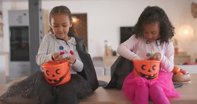 African American female children reaching into Halloween buckets on kitchen island, comparing candy