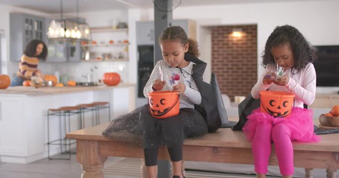 Mom with two child girls preparing pumpkins in kitchen; girls holding buckets pulling candy
