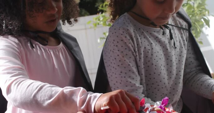 African American child girls in capes reaching into bowl on porch as adult holding sharing candy