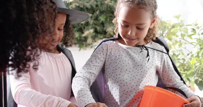 African American girl kids reaching into candy bowl held by adult on porch, filling pumpkin buckets