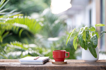 Red coffee cup and notebook and pencil with philodendron plant on wooden table © paladin1212