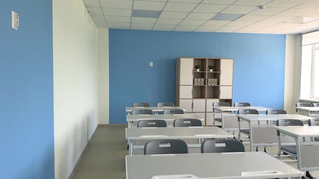 An empty school classroom in blue tones with gray desks.
