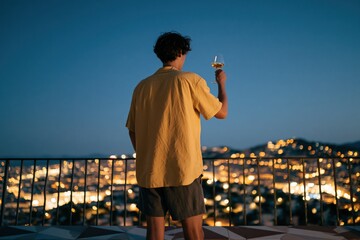 Obraz premium Man toasting overlooking city lights at dusk rooftop skyline background for celebration banner and urban lifestyle design