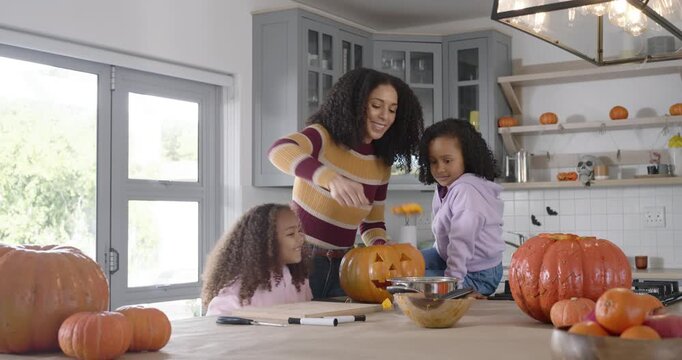 African-American mother and school-age girls carving pumpkin for fall in kitchen  and  scooping seed