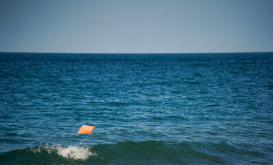 Orange safety buoy floating on calm deep blue sea waves under a bright sunny sky, offering a tranquil maritime scene with navigational safety concept. © samy
