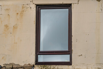 Fototapeta premium Rectangular, dark brown framed window centered on a light pinkish-beige, weathered exterior wall. The surface signs of age, wear, including water stains, areas of peeling paint, discolored patches. 