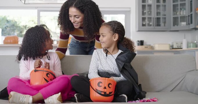 African American mom coming from kitchen, leaning over sofa handing pumpkin pails and helping girls
