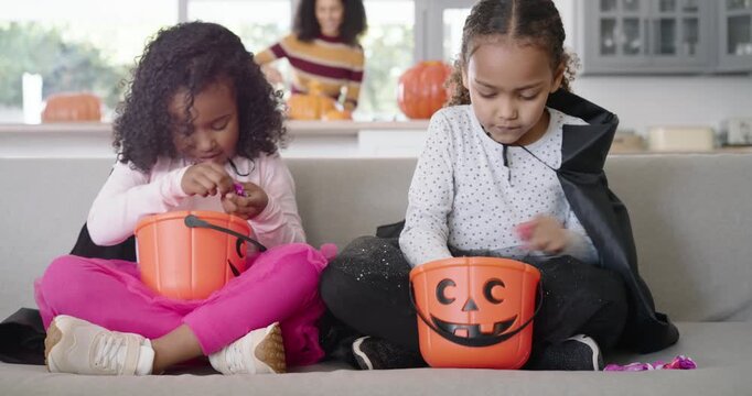 After Halloween haul African American girls sorting candy in pumpkin pails on couch