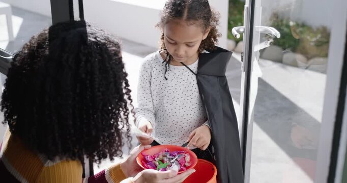 African American woman and girl sharing bowl at doorstep, girl filling pumpkin bucket walking away