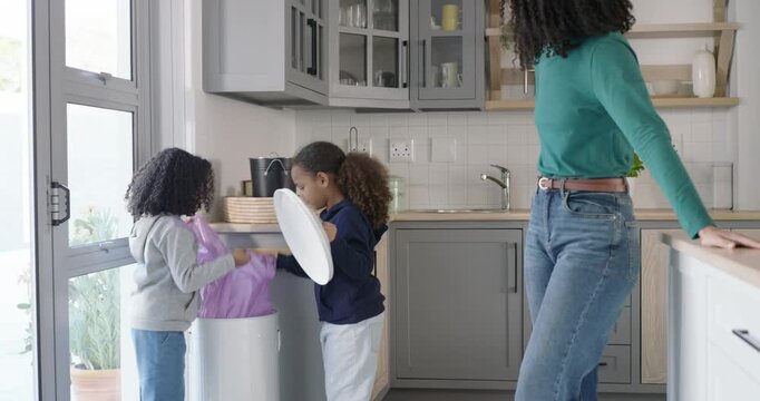 African-American mom guiding 2 girls lifting lid, replacing purple liner, sorting paper in kitchen