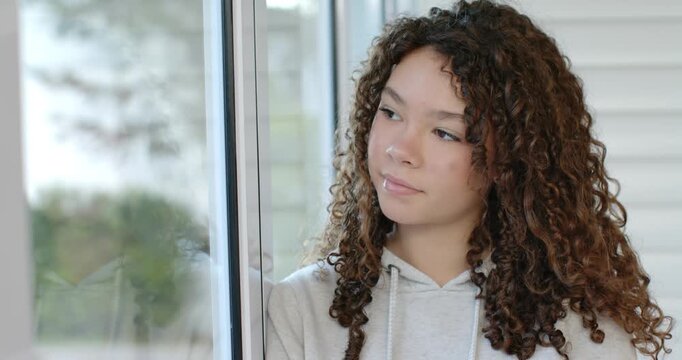 Teen African American girl looking out glass door turning to camera, noticing it, smiling in hoodie