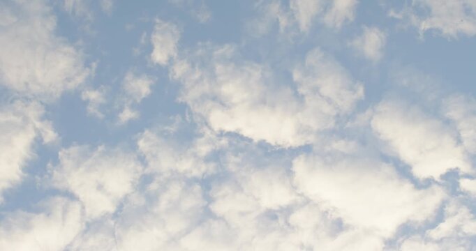Light breeze is stirring cloud field across pale blue sky, drifting and breaking, camera is tilting