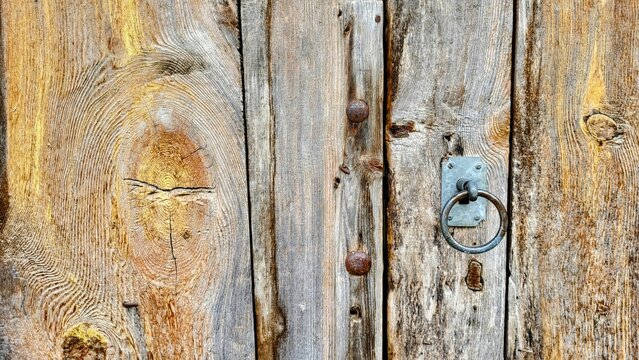Close-up of an old wooden door featuring a weathered metal lock in the Swiss Alps. Aged wood, worn metal and authentic surface textures convey rustic character and a sense of architectural history.