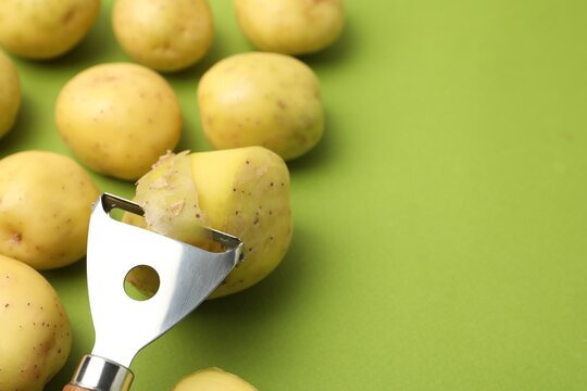 Ripe young potatoes and peeler on green background, closeup. Space for text