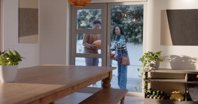 African American family approaching glass door, opening entry and bringing pumpkins inside