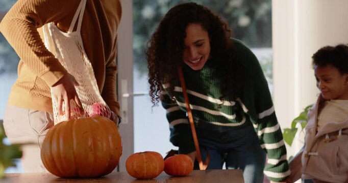 African American family entering doorway with mesh bag, unpacking pumpkins on table for fall