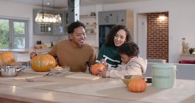 African American family guiding child marking small pumpkin at home for fall decor