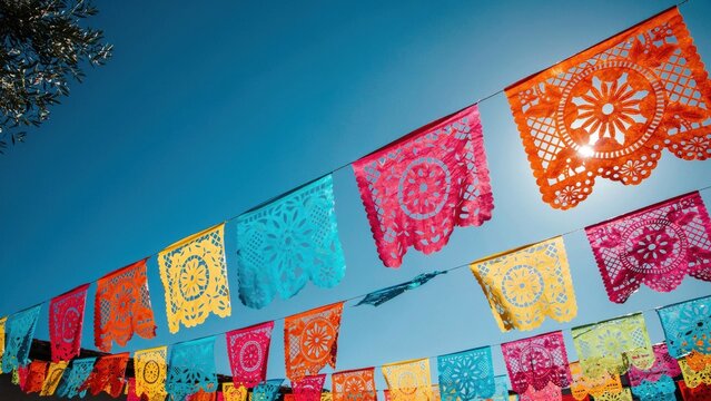 Colorful papel picado flags hanging against clear blue sky for festive decoration.