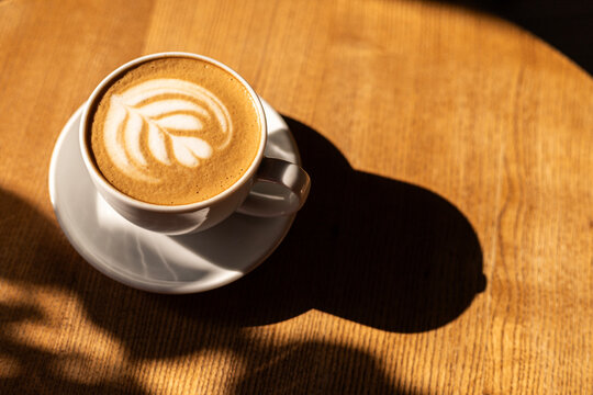 Latte art coffee cup on wooden table in warm sunlight