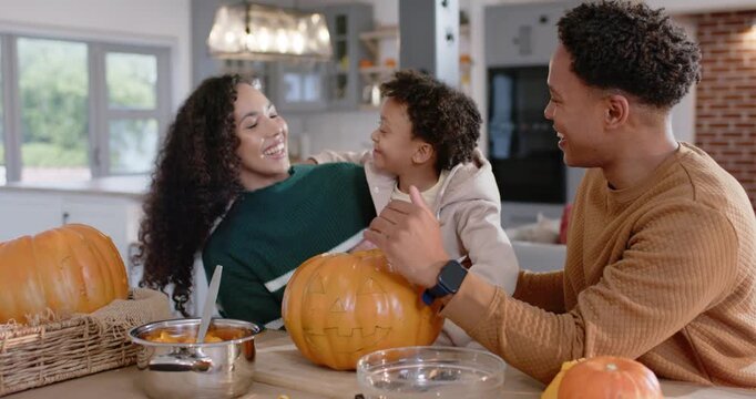 African American family carving large pumpkin at kitchen island, child reaching, sparking group hug