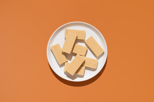 Wafer cookies on white plate against orange background