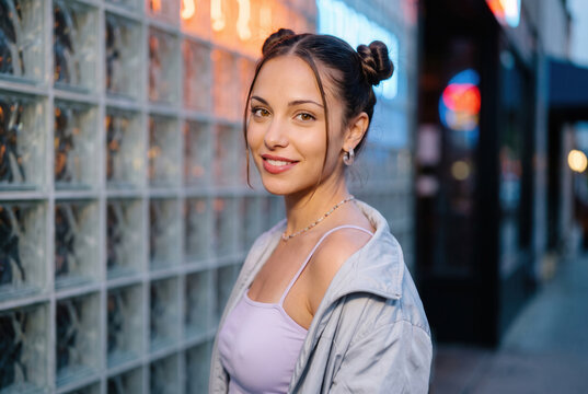 Woman with Twin Hair Buns in Early 2000s Style by a Glass Wall