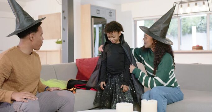 African family dressing female child for Halloween at home mom placing cape dad adjusting witch hat