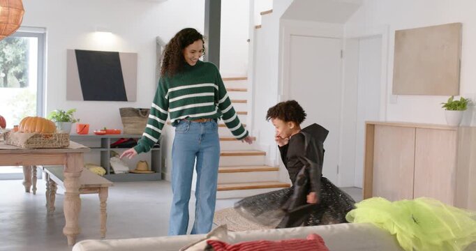 African American mom guiding spinning child wearing cape at home while man sorting pumpkin hat