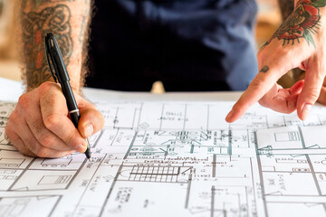 Tattooed hands examining architectural plans