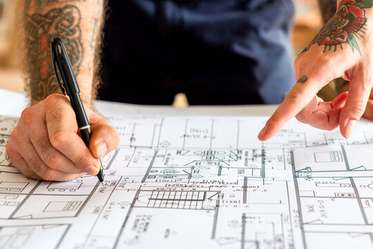 Tattooed hands examining architectural plans