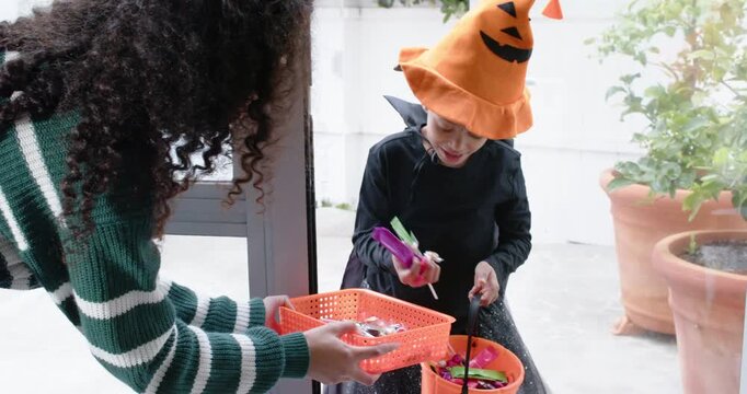 African American woman at door offering tray while child in costume filling pumpkin pail for treats