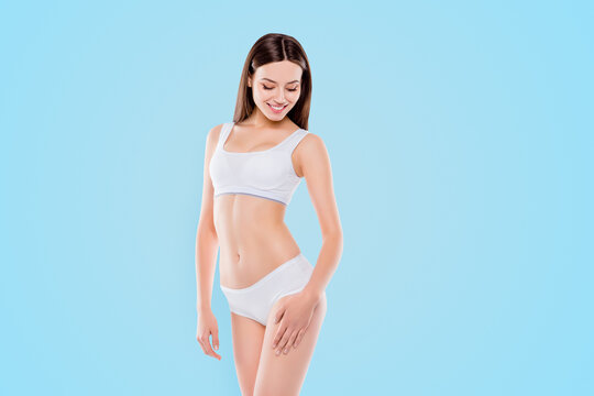 Portrait of thin sportive woman with perfect body in white cotton underwear bikini isolated over white background touching hips enjoying smooth ideal leg's skin