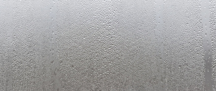 Water condensation droplets on a glass window. Rainy and foggy weather concept. Close-up of misty glass texture with running streaks