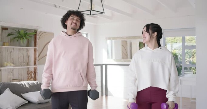 Couple doing biceps curls at home, man in pink hoodie straining with heavy dumbbells