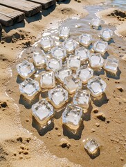 Fototapeta premium Ice cubes melt on a sandy beach near wooden planks and shallow water. Sunlight sparkles on the melting ice, suggesting cool refreshments on a warm day.