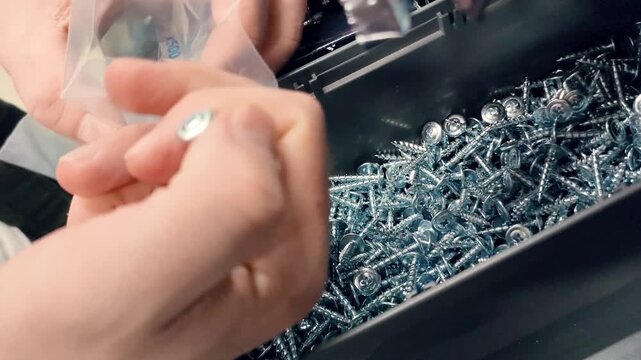 Close up of hands taking metal screws from a storage container and putting them into a small plastic bag in a hardware shop or workshop setting.High quality 4k footage