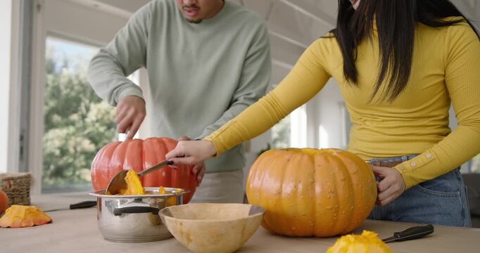 Couple cutting, scooping pumpkins in kitchen after removing lids, ladling pulp into pot for carving