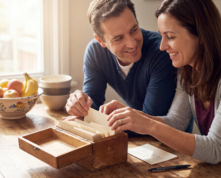 Adult siblings sorting recipe cards into a wooden recipe box at a kitchen table