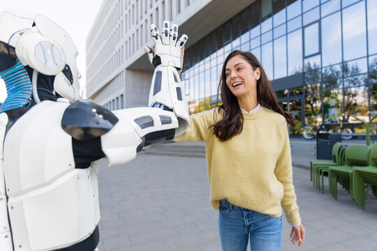 Smiling young woman giving high five to white humanoid robot