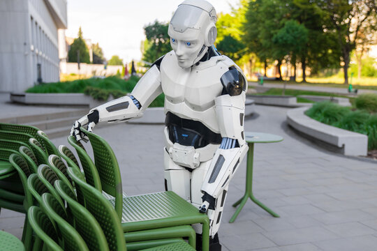 White android robot handling stacked chairs