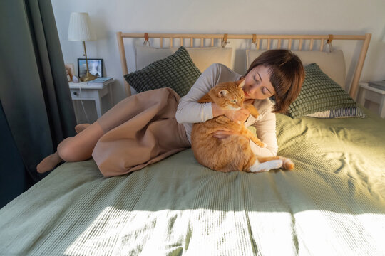 Woman cuddling ginger cat on bed in cozy bedroom