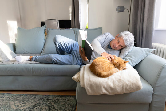 Senior man relax at home with ginger cat on sofa