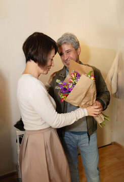 Smiling man gives flower bouquet to woman at home