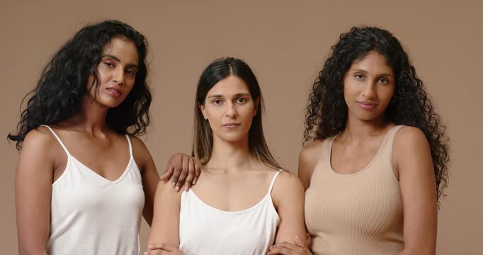 Diverse female models in tank tops posing after camera cue for studio with seamless beige backdrop